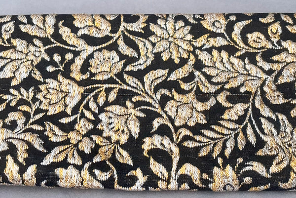 Back detail view of 1960s vintage black, gold, and silver metallic floral brocade long evening clutch purse with foldout chain handle. Showing a snag or pulled thread in the brocade fabric.