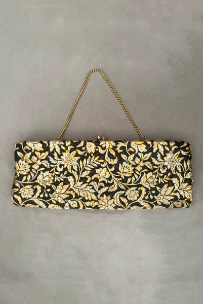Vertical front view of 1960s vintage black, gold, and silver metallic floral brocade long evening clutch purse with foldout chain handle. Showing the chain handle folded out.