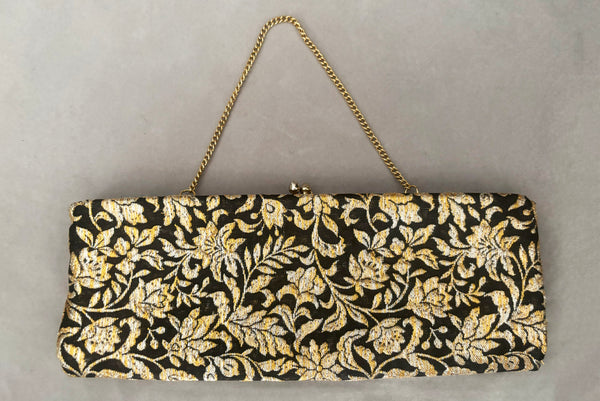 Horizontal front view of 1960s vintage black, gold, and silver metallic floral brocade long evening clutch purse with foldout chain handle. Showing the chain handle folded out.