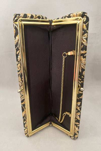 Vertical interior view of 1960s vintage black, gold, and silver metallic floral brocade long evening clutch purse with foldout chain handle. Showing the interior with its black synthetic lining.