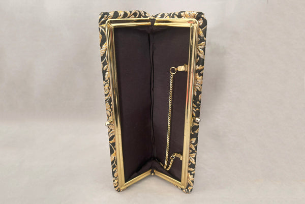 Horizontal interior view of 1960s vintage black, gold, and silver metallic floral brocade long evening clutch purse with foldout chain handle. Showing the interior with its black synthetic lining.