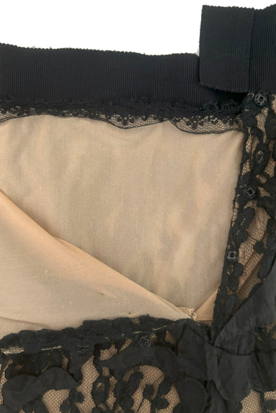 May include: A black lace skirt with a nude lining. The skirt has a black elastic waistband and a black satin bow at the back.