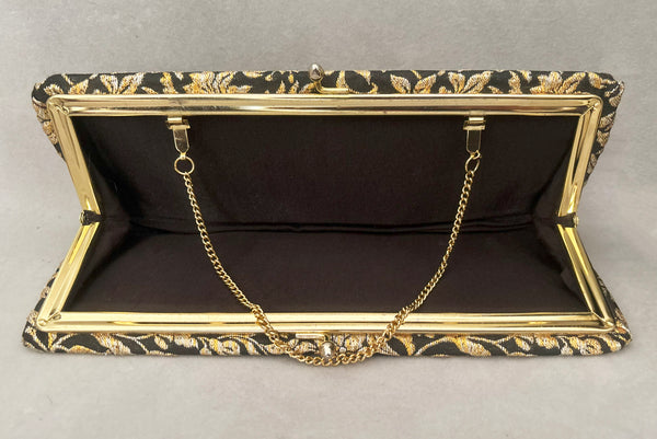 Horizontal interior view of 1960s vintage black, gold, and silver metallic floral brocade long evening clutch purse with foldout chain handle. Showing the interior with its black synthetic lining.