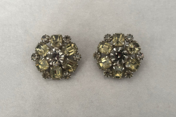 Horizontal front view of 1950s vintage smoke gray rhinestone and silver tone metal round clip-on earrings by Weiss.