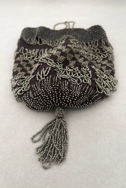 Vertical bottom view of 1910s turn of the century vintage Edwardian silver gray beaded black crochet drawstring handbag. Showing a close-up of the beaded tassel.
