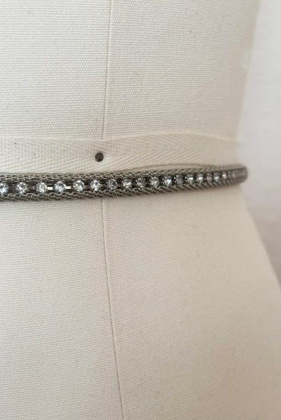 Detail view of 1960s vintage adjustable silver tone metal mesh and rhinestone chain belt with floral hook, size medium to large. Showing a close up of the metal mesh with a line of clear round rhinestones in the center.