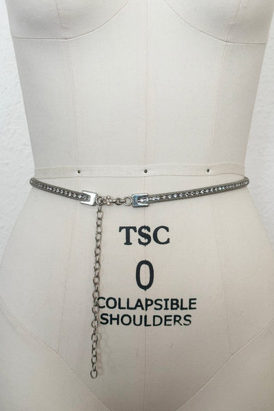 Vertical front view of 1960s vintage adjustable silver tone metal mesh and rhinestone chain belt with floral hook, size medium to large.