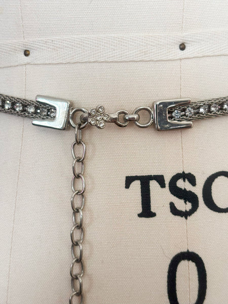 Detail view of 1960s vintage adjustable silver tone metal mesh and rhinestone chain belt with floral hook, size medium to large. Showing the adjustable chain and silver tone rhinestone floral hook closure.