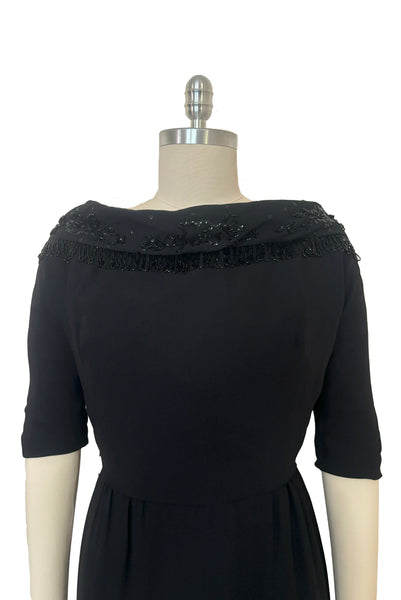 Bodice front view of 1960s vintage black fringe beaded and sequin boat neckline with standing collar cocktail dress by Elissa of California, medium to large. With V back, elbow length sleeves and pencil skirt.