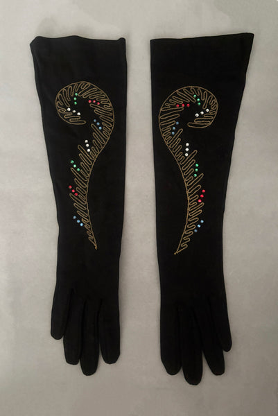 Vertical front view of 1950s vintage black mid length gloves with clear, red, blue, & green prong set rhinestone and gold work embroidery by Lady Gay, size 7.