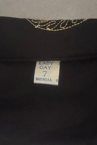 Interior detail view of 1950s vintage black mid length gloves with clear, red, blue, & green prong set rhinestone and gold work embroidery by Lady Gay, size 7. Showing the Lady Gay, size 7 label.