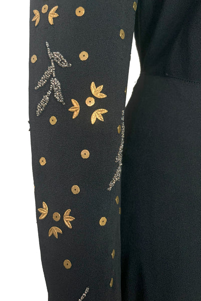 Sleeve detail view of 1930s vintage black rayon crepe evening gown with statement sleeves beaded with glass beads and brass sequins, small to medium. Showing the brass leaves and sequins, and pewter gray glass beaded leaves.