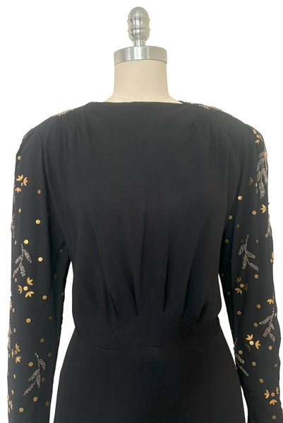 Bodice front view of 1930s vintage black rayon crepe evening gown with statement sleeves beaded with glass beads and brass sequins, small to medium. Showing the gathered shoulders, straight neckline, and pleated waist.
