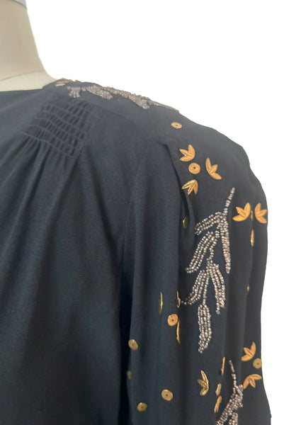 Shoulder detail view of 1930s vintage black rayon crepe evening gown with statement sleeves beaded with glass beads and brass sequins, small to medium. Showing the gathered shoulders, brass leaves and sequins, and pewter gray glass beaded leaves.