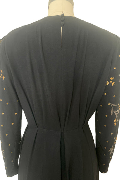 Bodice back view of 1930s vintage black rayon crepe evening gown with statement sleeves beaded with glass beads and brass sequins, small to medium. Showing the self-covered, three button closure and pleated waist.
