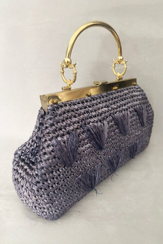 Vertical perspective view of 1950s periwinkle blue crochet raffia straw handbag with ornate gold tone metal handle, by Simon, made in Japan.