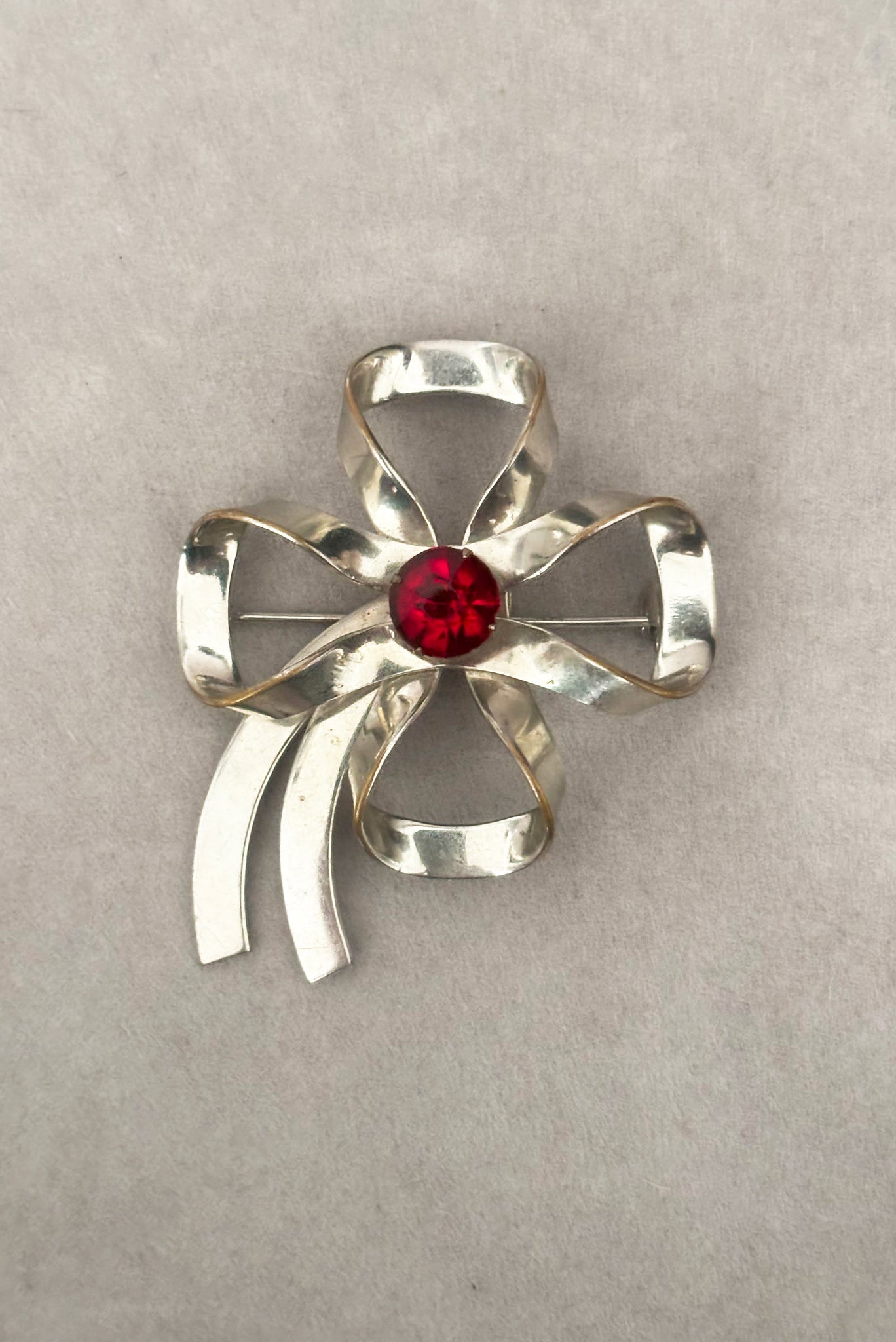 Vertical front view of 1950s vintage silver tone and round red rhinestone bow/ribbon brooch.