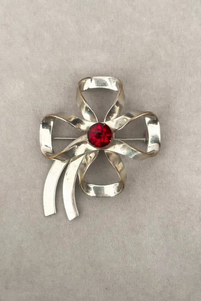 Vertical front view of 1950s vintage silver tone and round red rhinestone bow/ribbon brooch.