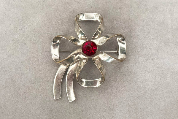 Horizontal front view of 1950s vintage silver tone and round red rhinestone bow/ribbon brooch.