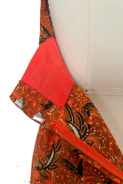 Detail view of hook, zipper, and lining on 1970s vintage orange and black Halloween bat and spider wax print cotton maxi dress with halter neckline, extra small to small.