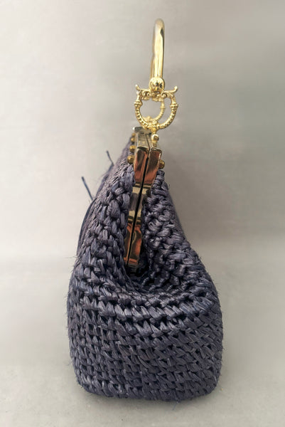 Vertical side view of 1950s periwinkle blue crochet raffia straw handbag with ornate gold tone metal handle, by Simon, made in Japan.