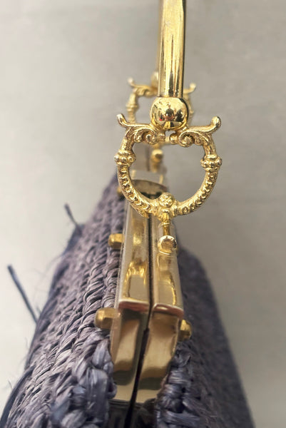 Detail view of 1950s periwinkle blue crochet raffia straw handbag with ornate gold tone metal handle, by Simon, made in Japan. Showing a close-up of the gold tone metal frame and ornate handle.