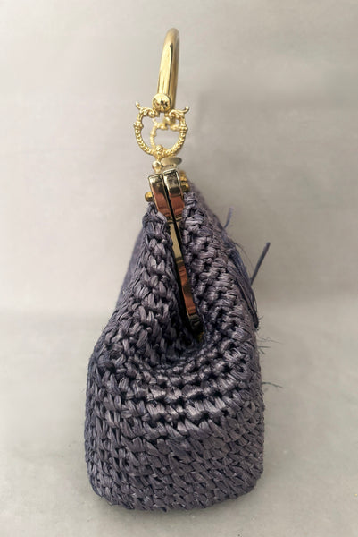 Vertical side view of 1950s periwinkle blue crochet raffia straw handbag with ornate gold tone metal handle, by Simon, made in Japan.