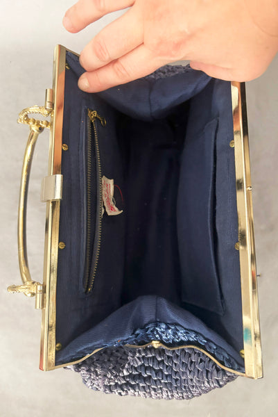 Detail view of 1950s periwinkle blue crochet raffia straw handbag with ornate gold tone metal handle, by Simon, made in Japan. Showing the blue fabric interior.