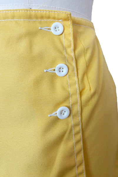 Detail view of 1960s vintage Koret of California Koratron yellow fabric skort with white plastic buttons, size medium to large. Showing a close up of the three white buttons on the front flap closure.