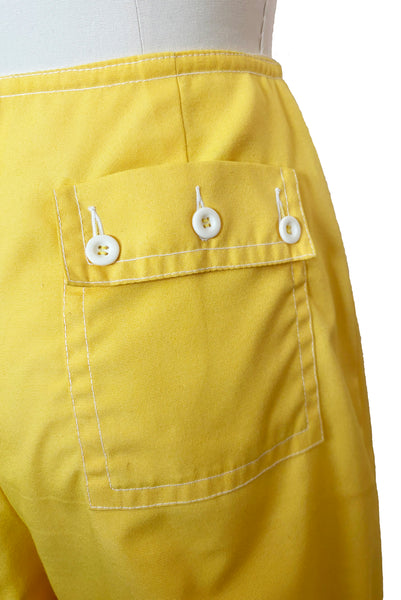 Detail view of 1960s vintage Koret of California Koratron yellow fabric skort with white plastic buttons, size medium to large. Showing a close up of the back pocket with three white button closure.