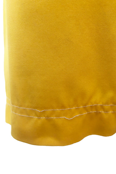 Detail view of 1960s vintage Koret of California Koratron yellow fabric skort with white plastic buttons, size medium to large. Showing a tiny spot near the hem and snapped topstitching.