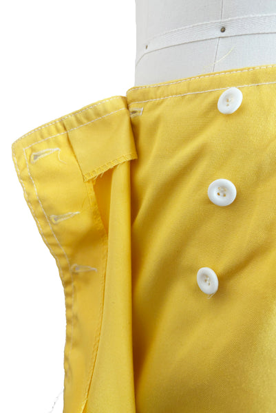 Detail view of 1960s vintage Koret of California Koratron yellow fabric skort with white plastic buttons, size medium to large. Showing a close up of the front button closure.