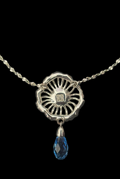 Detail view of early 2000s vintage silver tone, blue opaline rhinestone, and crystal floral adjustable necklace and pierced stud earrings jewelry set by Givenchy. Showing the back of the necklace pendant marked with the Givenchy stamp.