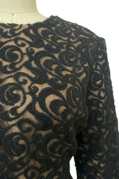 Front bodice detail view of 1990s vintage Balmain Ivoire long sleeve nude look black wool lace cocktail dress with draped wool crepe skirt, small to medium. Showing the swirl pattern black wool lace with beige lining for a nude look.