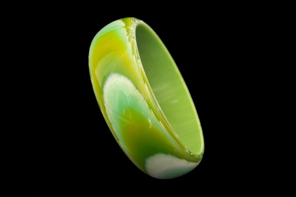 Horizontal perspective view of 1960s vintage green, chartreuse, and white feathered Lucite plastic domed bangle bracelet.