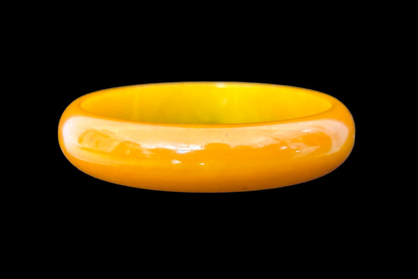 Horizontal front view of 1940s vintage egg yolk and butterscotch mustard yellow marbled Bakelite domed bangle bracelet.