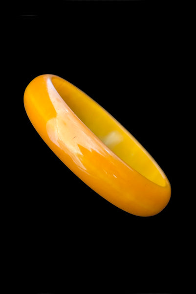Vertical perspective view of 1940s vintage egg yolk and butterscotch mustard yellow marbled Bakelite domed bangle bracelet.