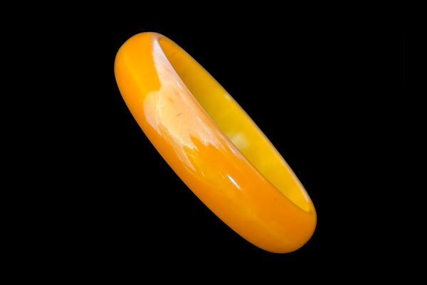 Horizontal perspective view of 1940s vintage egg yolk and butterscotch mustard yellow marbled Bakelite domed bangle bracelet.