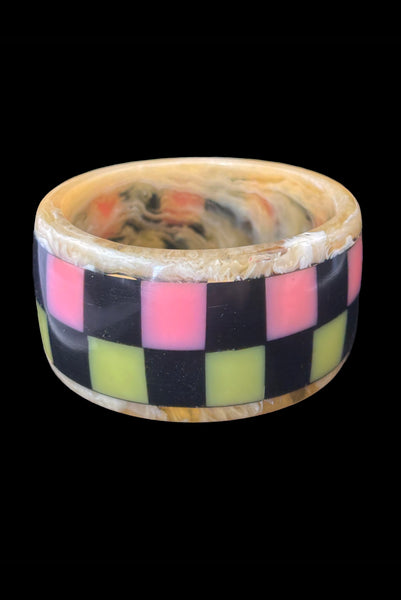 Vertical front view of 1960s vintage artisan lime green, pink, and black inlaid checkerboard Lucite bangle bracelet on a translucent marbled beige base.