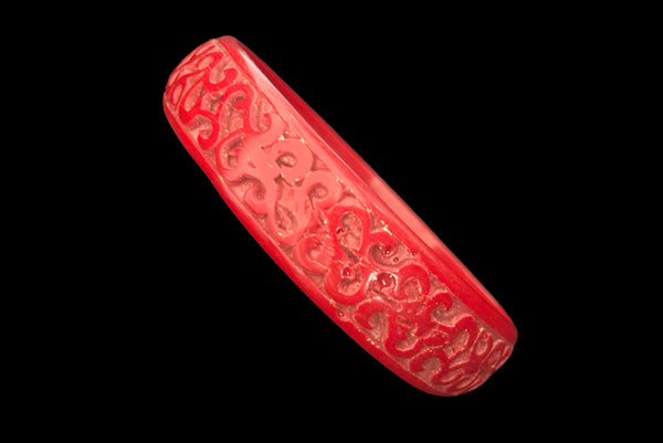 Horizontal perspective view of 1950s vintage red cinnabar scroll carved lacquered Asian bangle bracelet. Showing a close-up of the area where the carving isn't as fine.