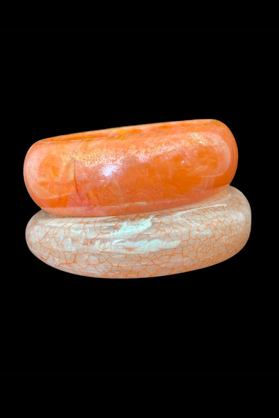 Vertical front view of 1980s iridescent orange and crackled orange and white plastic bangle bracelet set of two (2).