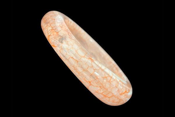 Horizontal perspective view of 1980s iridescent orange and crackled orange and white plastic bangle bracelet set of two (2). Showing the asymmetrical orange and white crackled bangle.