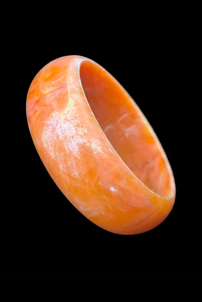 Vertical perspective view of 1980s iridescent orange and crackled orange and white plastic bangle bracelet set of two (2). Showing the iridescent domed bangle.