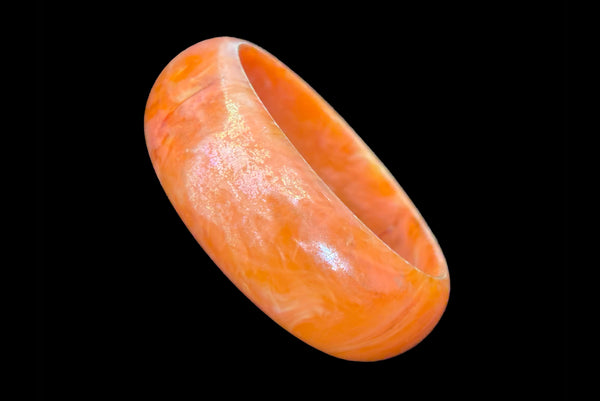 Horizontal perspective view of 1980s iridescent orange and crackled orange and white plastic bangle bracelet set of two (2). Showing the iridescent domed bangle.