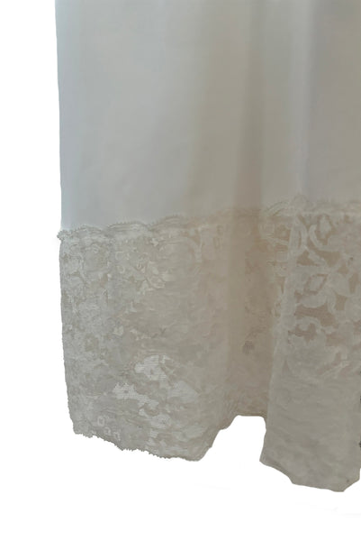 Skirt detail view of 1950s vintage white sheer lace sweetheart neckline full slip by Vanity Fair, small to medium. Showing deep floral patterned lace trim at the hem.