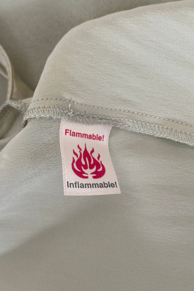 Interior detail view of 2000s y2k vintage new with tags sage green silk charmeuse robe by Patricia Fieldwalker, size medium to large. Showing the flammable tag.