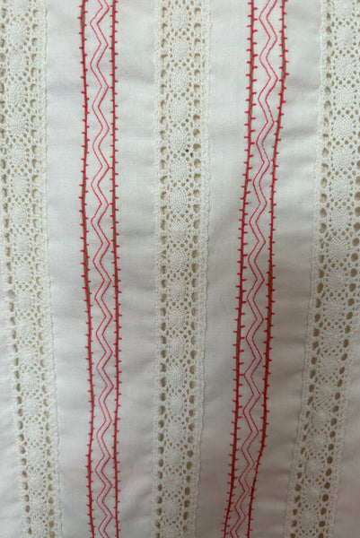 Detail view of 1950s vintage white cotton scoop neck, button front, gathered half sleeve, pleated skirt peasant dress with red embroidery, size small to medium. Showing a close up of the white cotton with insertion lace and red zig zag embroidery.