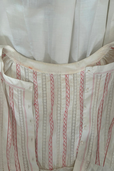 Interior detail view of 1950s vintage white cotton scoop neck, button front, gathered half sleeve, pleated skirt peasant dress with red embroidery, size small to medium. Showing some discoloration inside the back neckline.