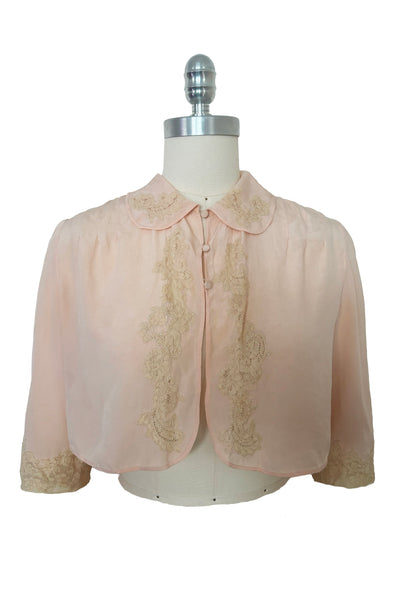 Front view of 1930s vintage blush pink silk cream lace trimmed peter pan collared bed jacket, size extra small to small.