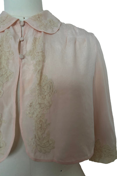 Detail view of 1930s vintage blush pink silk cream lace trimmed peter pan collared bed jacket, size extra small to small. Showing the inset lace appliques and three button close.